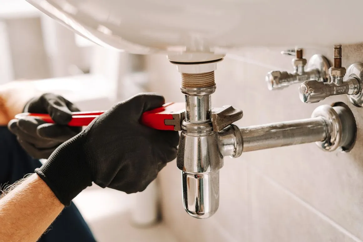 Technician repairing a sink pipe with a wrench